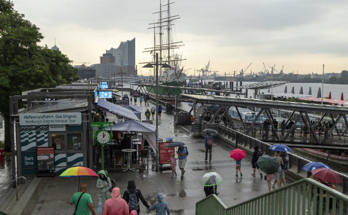Passanten mit Regenschirmen bei den Landungsbrücken in Hamburg: Regenfälle werden zunehmen. Mit einem GDV-Leitfaden können Hausbesitzer ihre Gebäude klimaresilienter bauen oder erneuern.