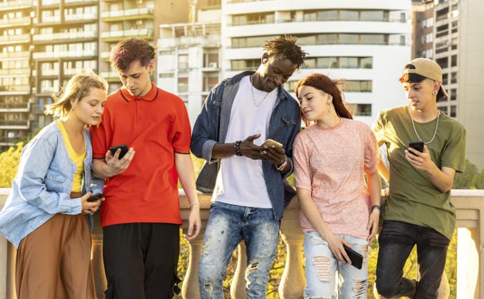 5 Jugendliche, die auf ihre Handys schauen: Auszubildende bringen eine hohe Medienkompetenz mit, die Versicherer für sich nutzen können.