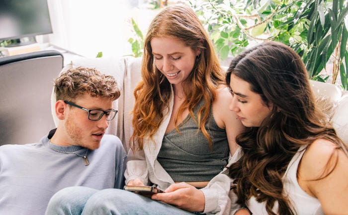 Drei Jugendliche schauen gemeinsam auf ein Handy: Viele junge Erwachsene folgen den Tipps von Finfluencern für ihre Geldanlage.