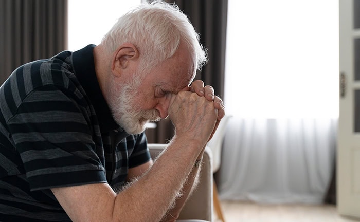 Trauernder Mann sitzt im Wohnzimmer und erhält Todesfallleistungen.