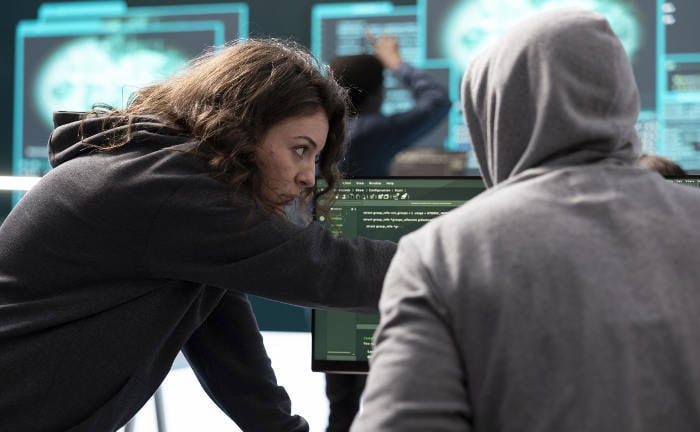 Frau arbeitet mit Kollegen an einem Quellcode: Cyberangriffe auf Firmen nehmen weiter zu.