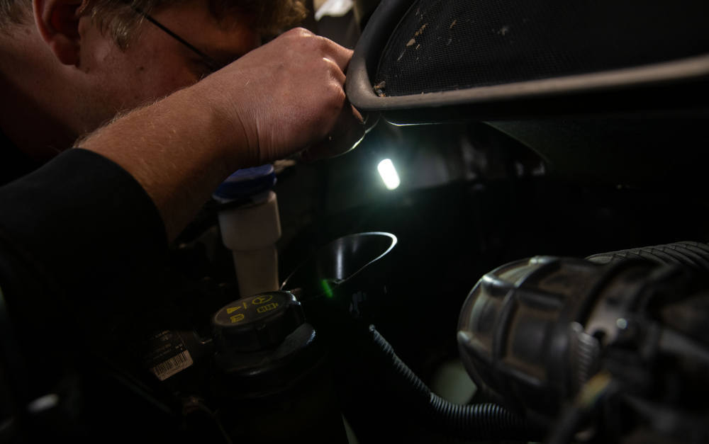 KFZ-Mechaniker leuchtet in der Autowerkstatt in einen Motorraum: Ziemlich duster sieht es auch auf der Kostenseite der KFZ-Haftpflichtversicherungen aus