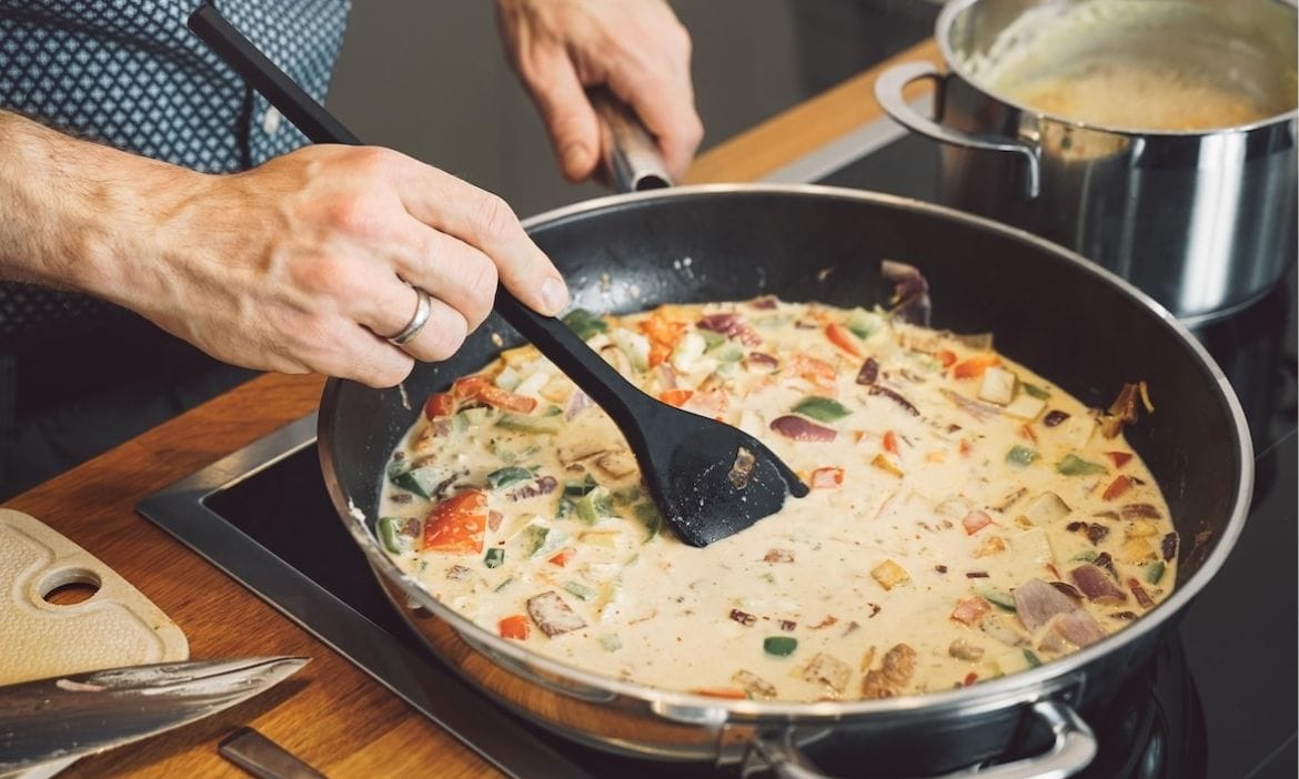 Mann kocht mit einer beschichteten Pfanne: Der GDV erweitert seine Musterbedingungen um PFAS-Chemikalien.