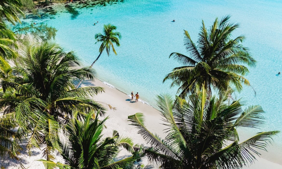 Zwei Personen an einem Sandstrand in Thailand: Eine Reiserücktrittsversicherung springt ein, wenn ein Urlaub unvorhergesehen ins Wasser fällt.