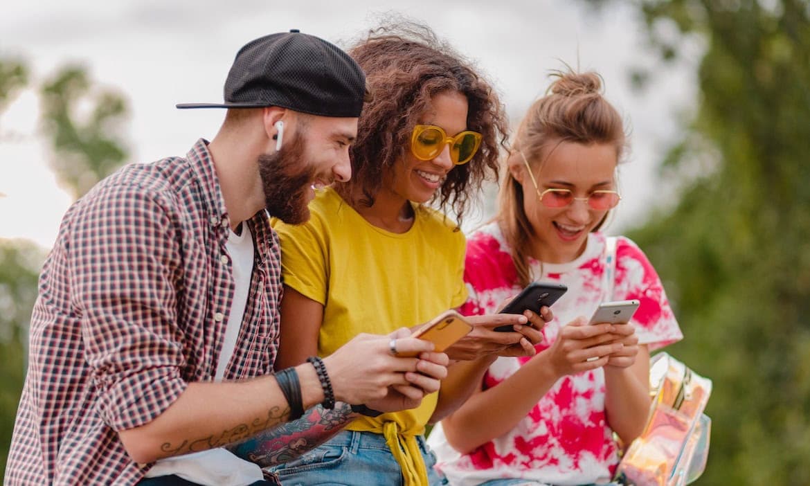 Junge Leute schauen auf ihr Smartphone: Junge Kunden nutzen gerne Versicherungs-Apps.